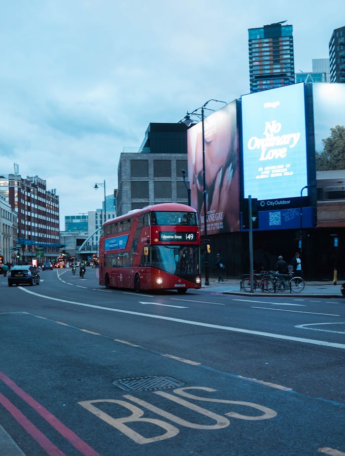services-01 A classic red double-decker bus driving through a bustling London street at dusk, with city lights illuminating the scene.
