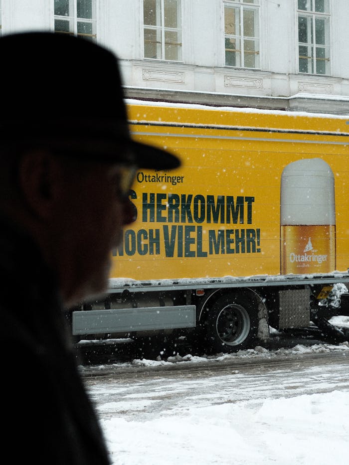 Silhouette of a man passing by a beer advertisement truck during a snowy winter day.