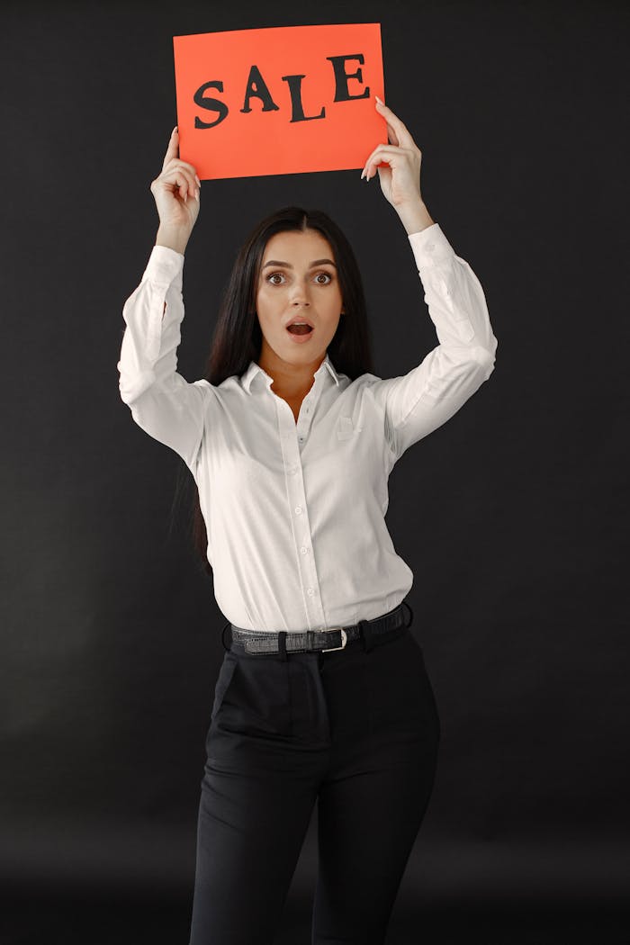 Professional woman in white shirt holding a sale sign with an expression of surprise.
