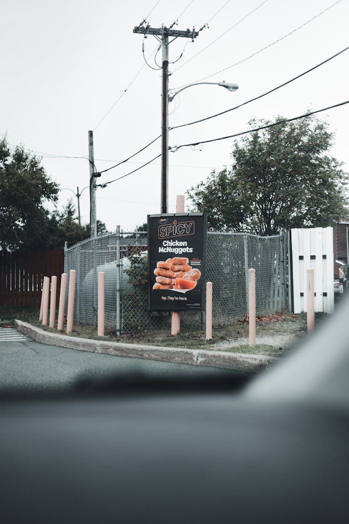 Outdoor signage featuring Spicy Chicken McNuggets beside a chain link fence and electric post.